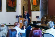 Mężczyzna w ciemnym garniturze przemawia za mównicą