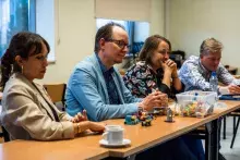 fot. Sebastian Jętczak/UG Czworo uczestników warsztatów siedzi w rzędzie przy stole. Wszyscy pochylają się nad stołem, patrząc na małe konstrukcje zbudowane z klocków Lego. Na stole widać również pojemnik z klockami i filiżankę.