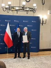 Dwóch mężczyzn stojących na granatowej ściance z napisem "ministerstwo spraw zagranicznych"