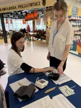 Zdjęcie przedstawiające dwie kobiety, jedną obsługującą urządzenie do mierzenia ciśnienia tętniczego, a drugą podlegającą badaniu