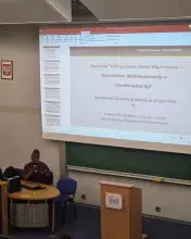 Widok na salę wykładową. Na dużym ekranie wyświetlany jest slajd tytułowy prezentacji: „'Speaking Truth to Power: Which Way Forward – Doctrinalism, Multidisciplinarity or Interdisciplinarity?'”. Pod tytułem informacja, że wykład wygłasza prof. Olu Ojedokun, rektor Protestant University of Rwanda, na Uniwersytecie Gdańskim, 23 kwietnia 2026 r. Po lewej stronie, przy stole, siedzi prelegent w bordowej szacie i tradycyjnym nakryciu głowy, mówiąc do mikrofonu.