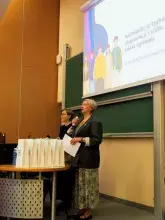 Zdjęcie przedstawiające 2 osoby stojące przed zielona tablicą kredową prowadzącą wykład