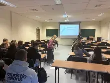 Zdjęcie przedstawiające grupę słuchaczy siedzących w płaskiej sali wykładowej