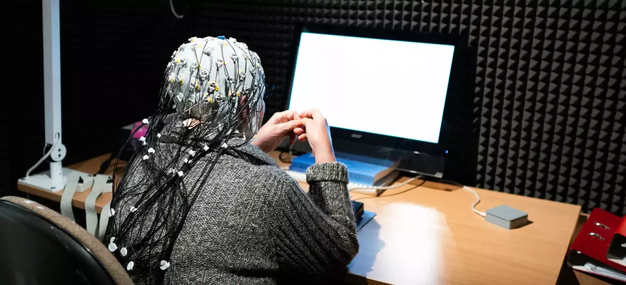 badanie przy użyciu EEG - widok od tyłu; starsza osoba z czepkiem z elektrodami na głowie, siedząca przed monitorem
