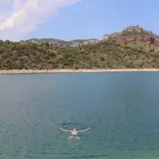 Pejzaż z widokiem z wody na pagórkowate wybrzerze, w centalnej części, w wodzie, człowiek pływający na plecach